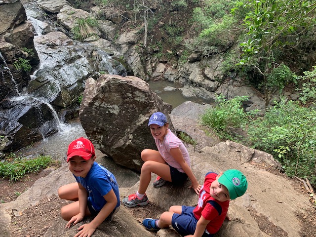 Rory, Poppy and Louie smile at the camera sitting next to a waterfall