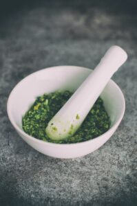 Close up of a white mortar and pestle with ground herbs