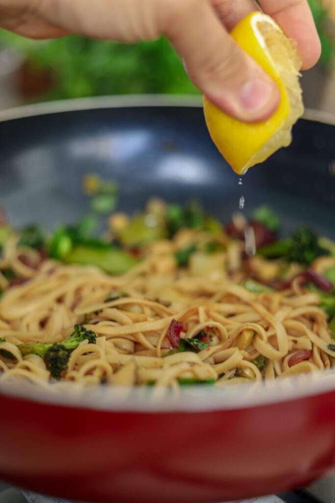 Close up image of a lemon being squeezed onto a bowl of pasta